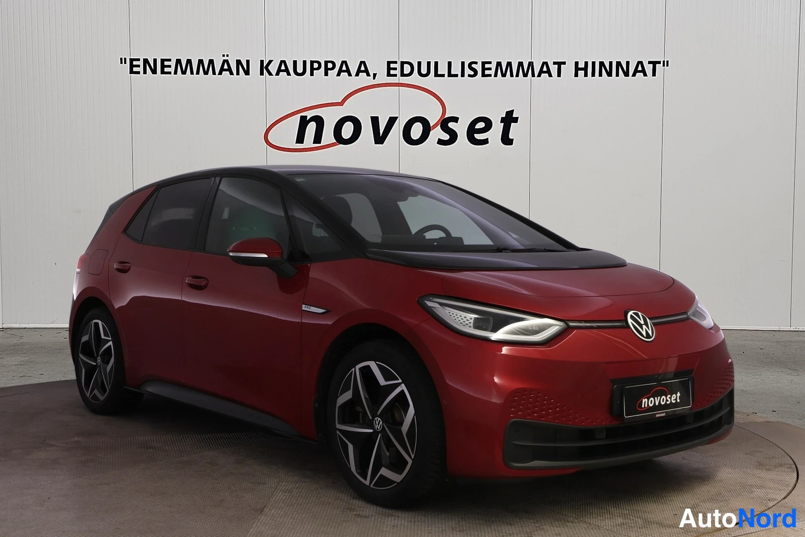 Etuviisto, nokka oikealle: Front three-quarter view of a red Volkswagen ID.3 from the right side, showing its headlights and alloy wheels.