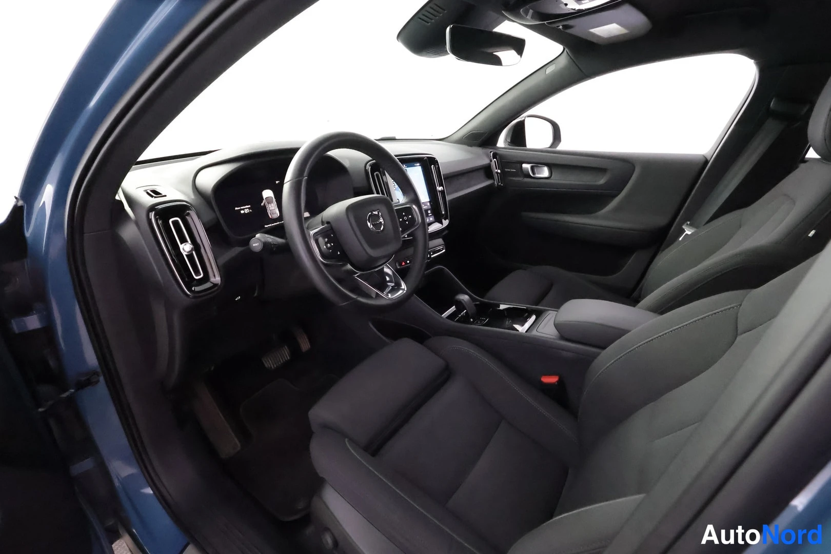 Muu: Volvo C40:n sisätila kuljettajan puolelta: tumma ohjaamo, ohjauspyörä ja keskikonsolin näyttö.