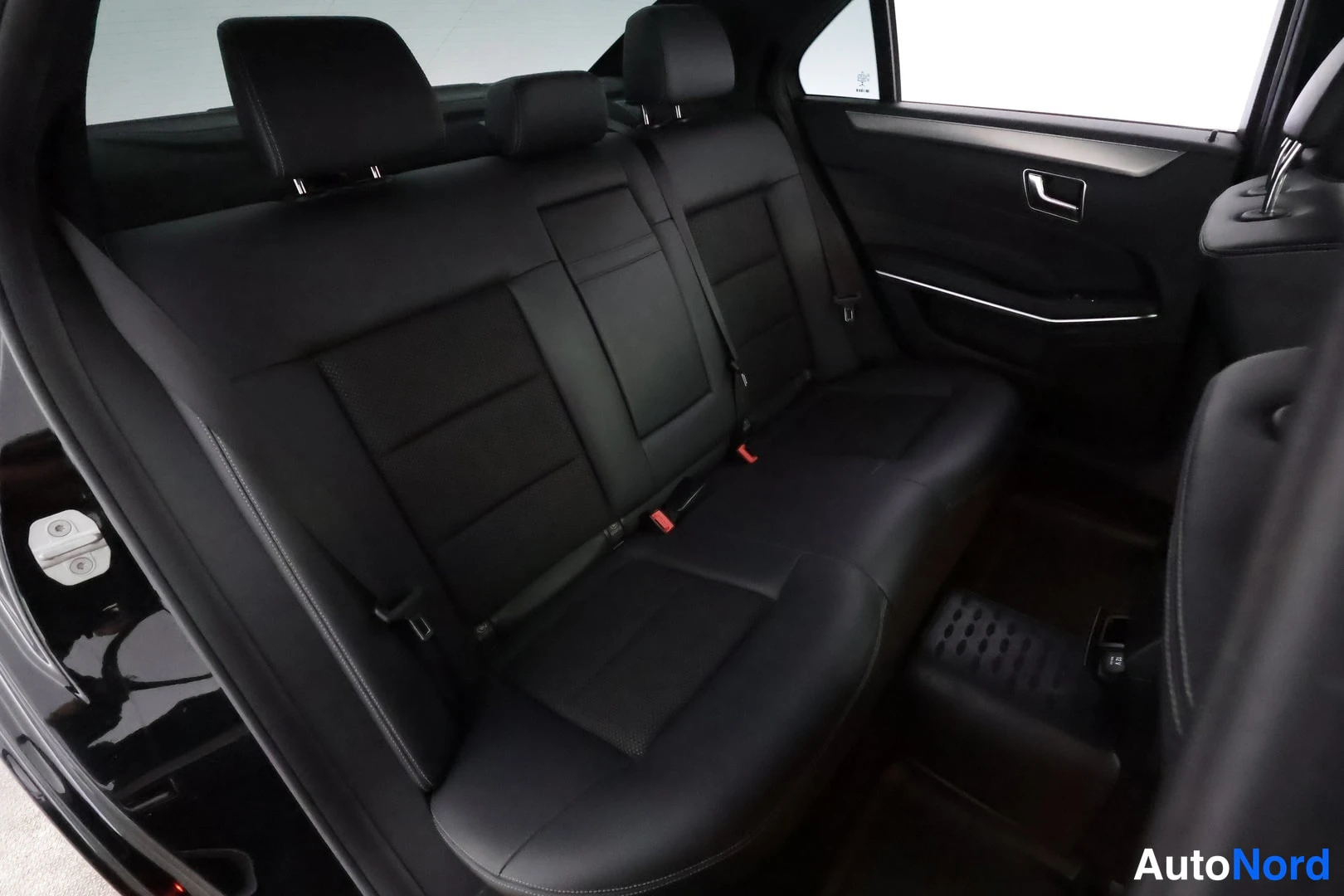 Muu: Takapenkki sivusta kuvattuna: musta kolmiosainen istuinosa, kaksiosainen selkänoja niskatuineen ja ovipaneeli, jonka kahvassa kirkas koriste.