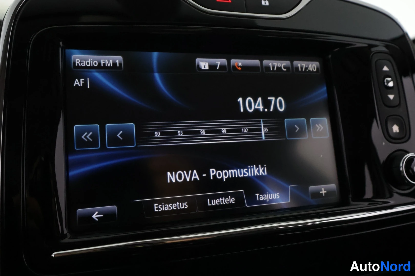 Muu: Kojetaulun kosketusnäyttö näyttää FM-radiota: taajuus 104.70, ohjelmalla lukee NOVA - Popmusiikki. Näytön oikealla reunassa on fyysisiä nuoli- ja kotipainikkeit