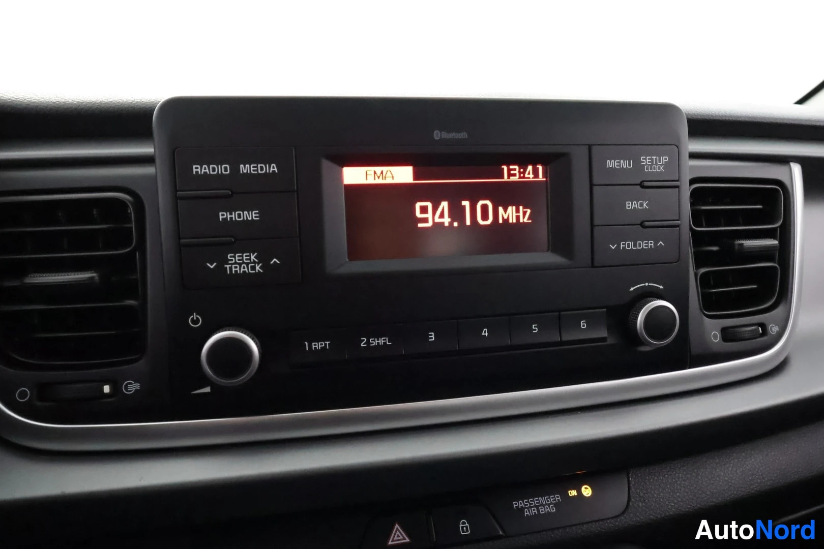Yksityiskohta: Auton radio: näytöllä FM 94.10 MHz ja kello 13:41, nappien keskellä Radio, Media, Phone.