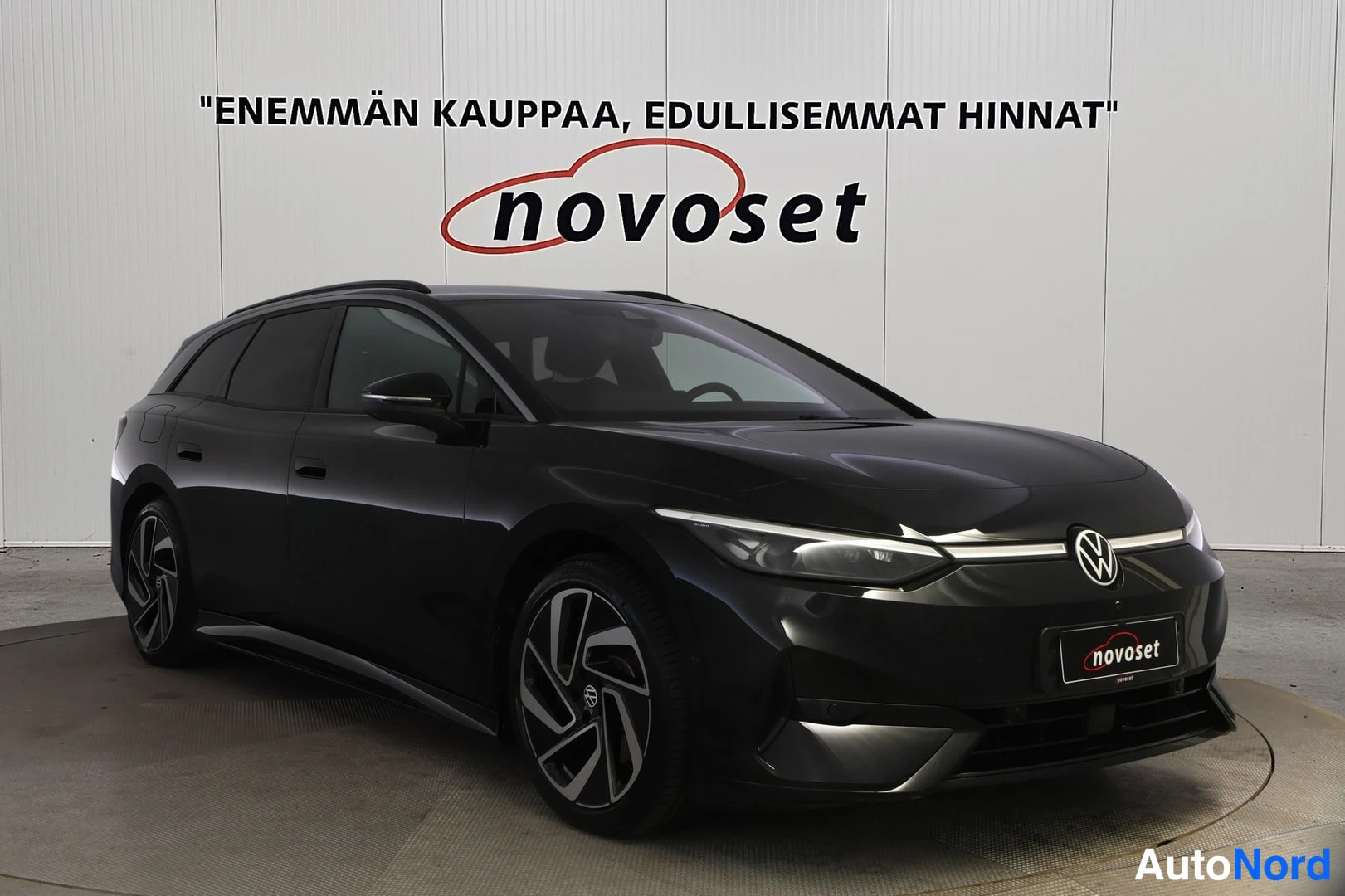 Etuviisto, nokka oikealle: Musta farmarimallinen henkilöauto kuvattuna etunurkkal: keula ja kylki näkyvät vaaleaa paneloitua taustaa vasten.