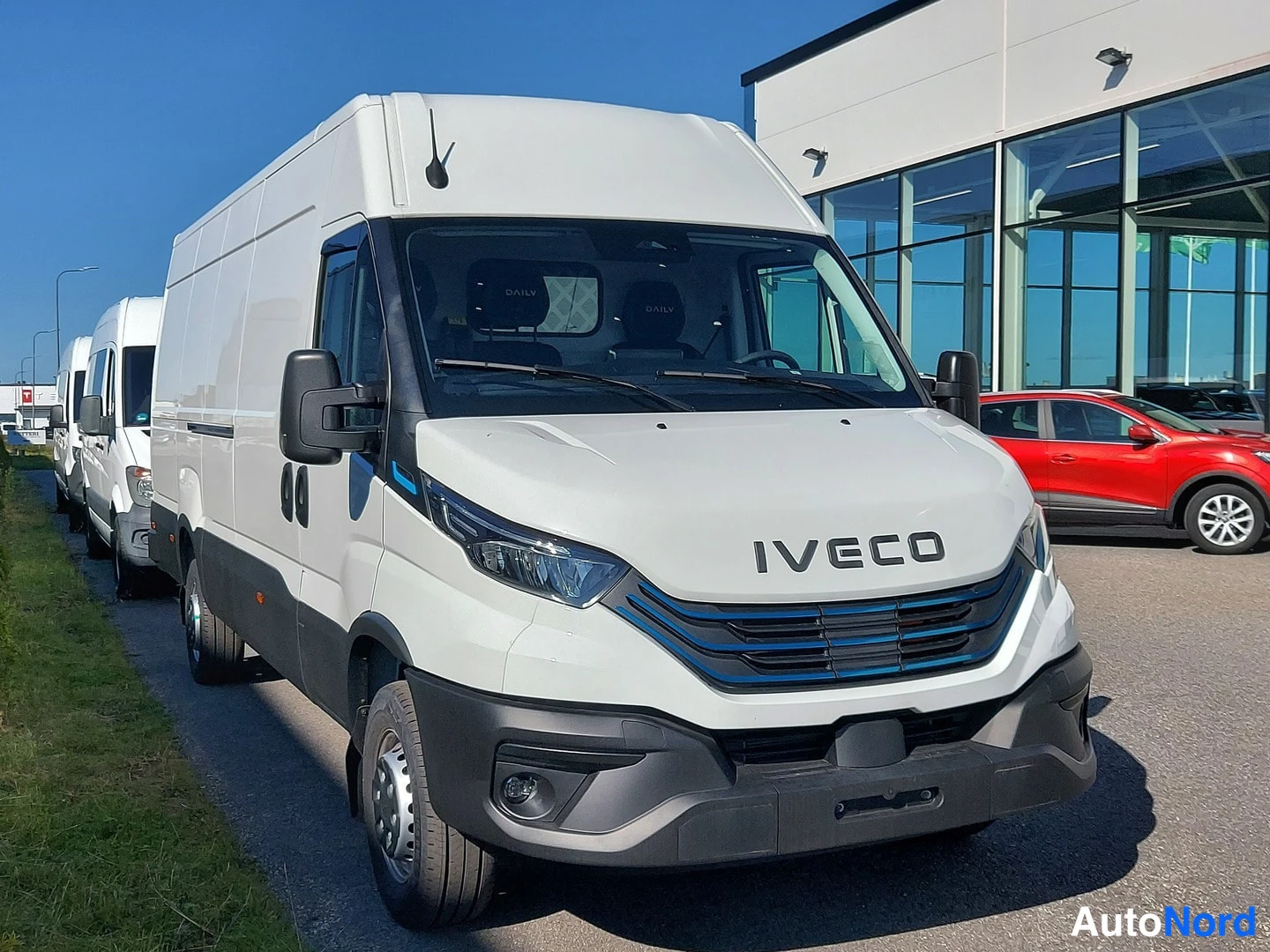 Etuviisto, nokka oikealle: Valkoinen Iveco Daily -pakettiauto etuviistosta, keula oikealla; IVECO-merkitty etusäleikkö, konepelti ja tuulilasi kuvan keskellä.