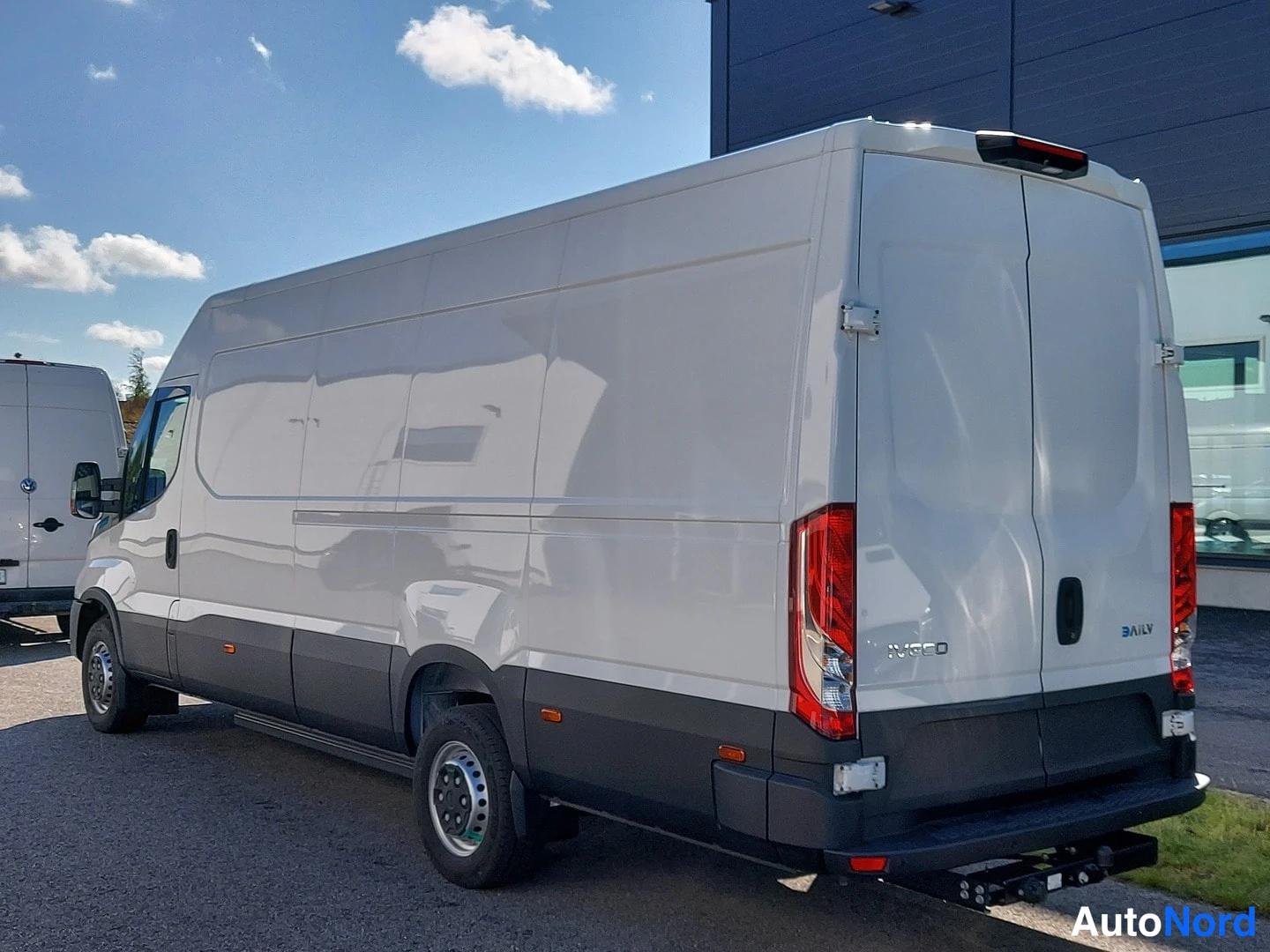 Takaviisto: Valkoinen Iveco Daily -pakettiauto takaviistosta, perä oikealla; punaiset pystytakavalot, DAILY-merkintä takaluukussa ja vetokoukku takapuskurissa.