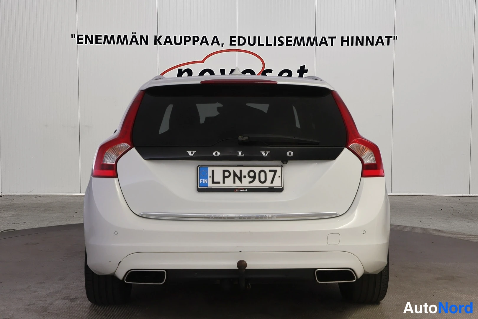 Takaa: Valkoisen farmarin suora takaosa; VOLVO-teksti takaluukussa, takanappi, kaksi pakoputkea ja irrotettava vetokoukun pallo puskurin alla.