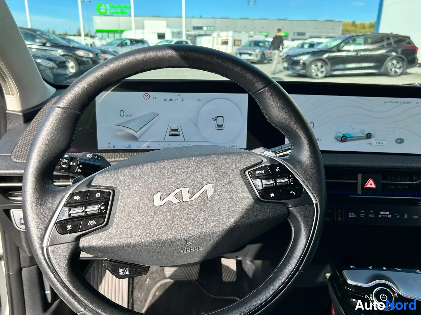 Sivulta: Kia-ohjauspyörä ja mittariston digitaalinäyttö, jossa näkyy pysäköintitila ja nopeusmerkki.