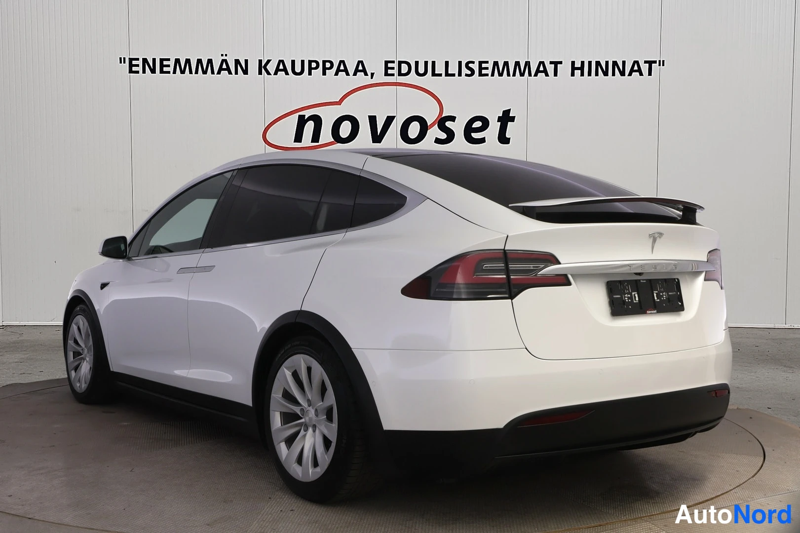 Takaviisto: Valkoinen Tesla Model X takaviistokuvassa, perä oikealla ja vasen kylki näkyvissä; tumma lasikatto, takaluukun spoileri ja mustat takavalot.