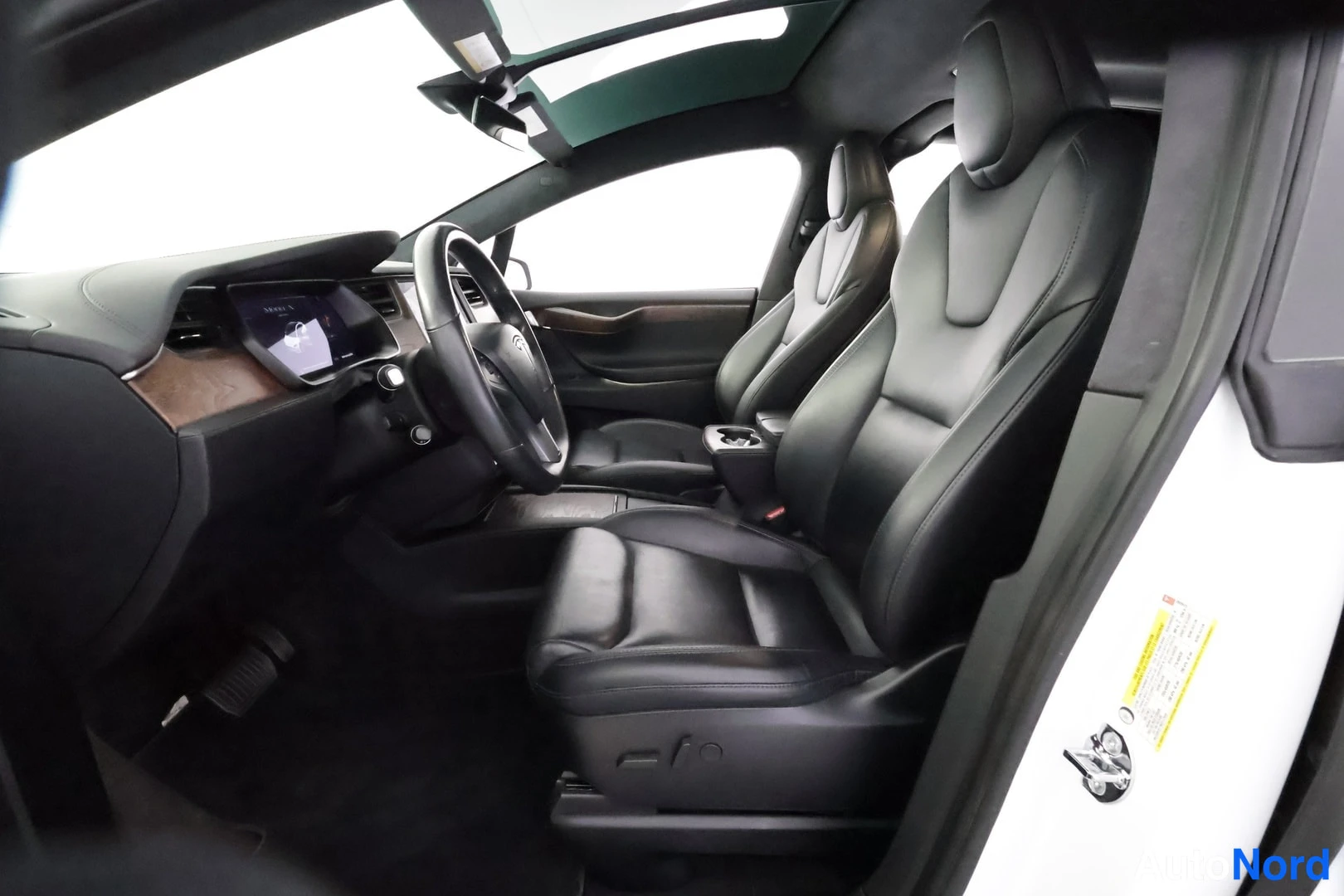 Etuviisto: Tesla Model X:n etuistuimet ja kojelauta ovista käsin kuvattuna: mustat nahkaistuimet, puukoristeet ja panoraamakatto.