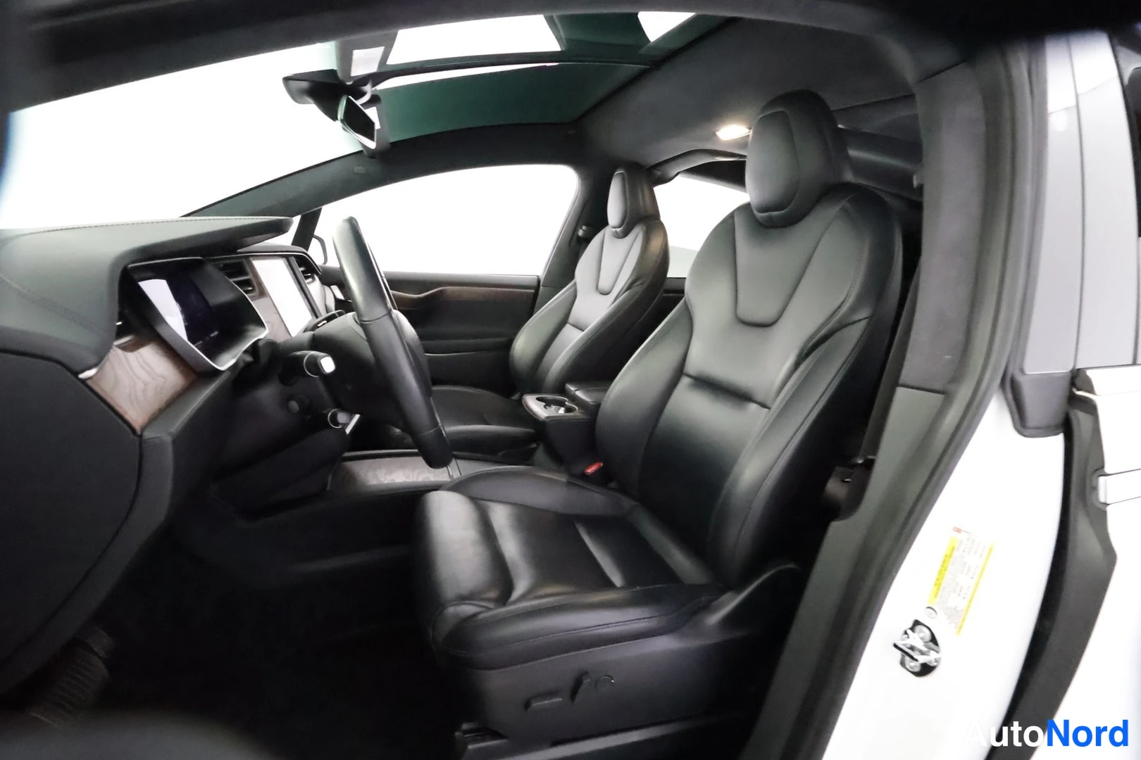 Etuviisto: Tesla Model X:n matkustamo kuljettajan ovesta kuvattuna: mustat nahkaistuimet, puukoristeinen kojelauta ja panoraamakatto.