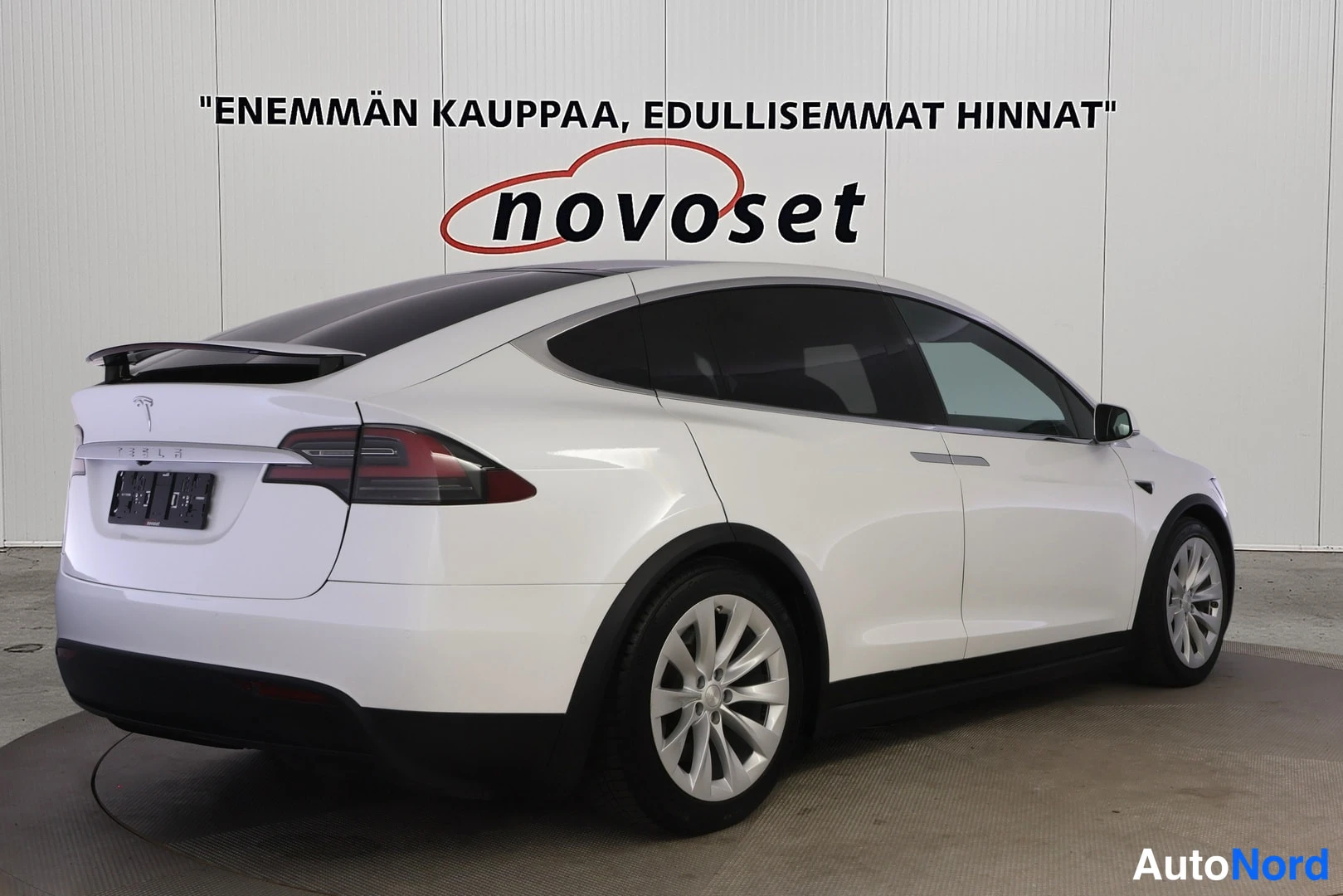 Takaviisto: Valkoinen Tesla Model X takaviistokuvassa, perä kuvan vasemmassa laidassa ja oikea kylki näkyvissä; tumma lasikatto ja hopeanväriset vanteet.