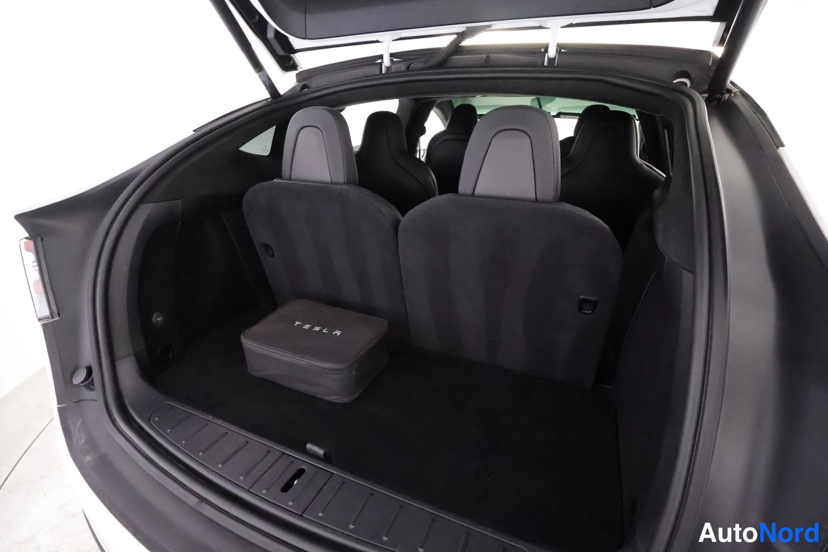 Muu: Avattu tavaratila, jonka lattialla on Tesla-merkitty laukku ja taaana käärittyjä takanojia.