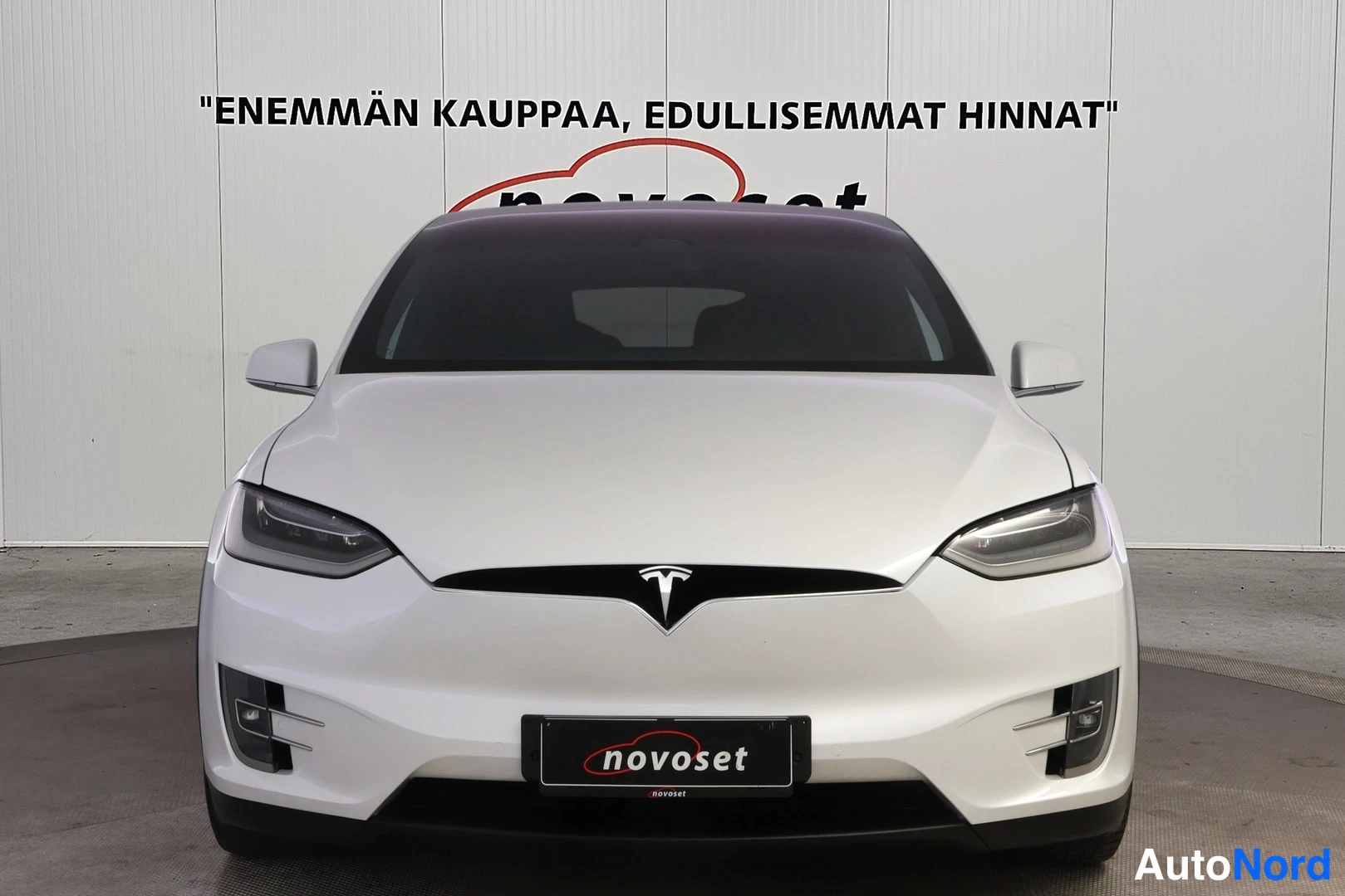 Edestä: Valkoisen Tesla Model X:n suora etunäkymä, keulakoriste ja Tesla-tunnus keskiössä.