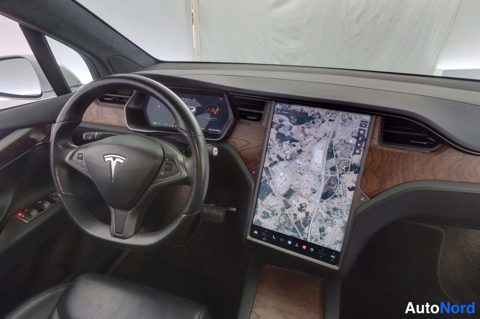 Muu: Tesla Model X:n ohjaamon lähikuva: ohjauspyörä, kuljettajan näyttö ja pystyyn asennettu karttanäyttö puukoristeisessa kojelaudassa.