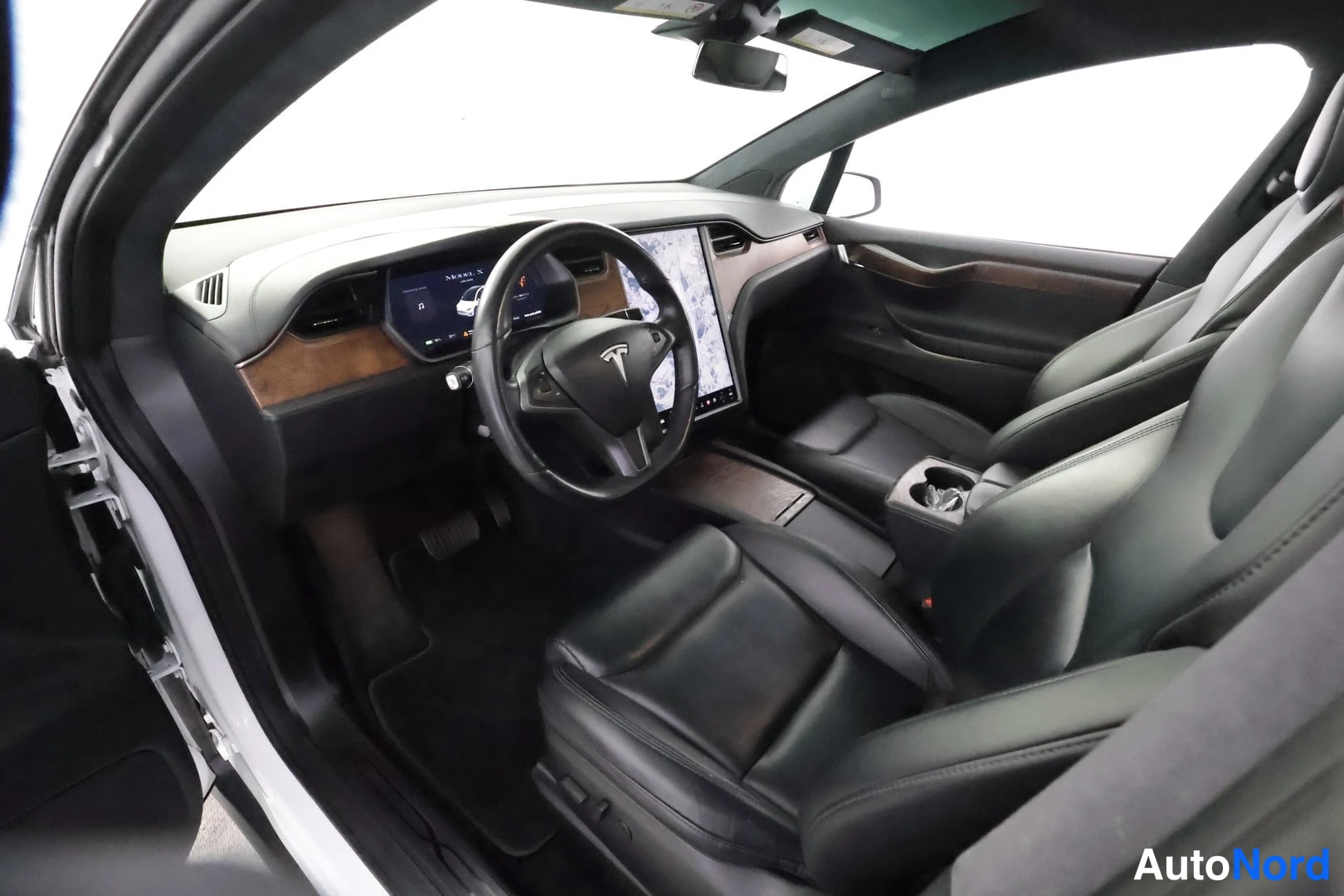 Etuviisto: Tesla Model X:n matkustamo kuljettajan puolelta kuvattuna: puukoristeinen kojelauta, Tesla-logolla varustettu ohjauspyörä, suuri keskinäyttö ja mustat nahkaistu