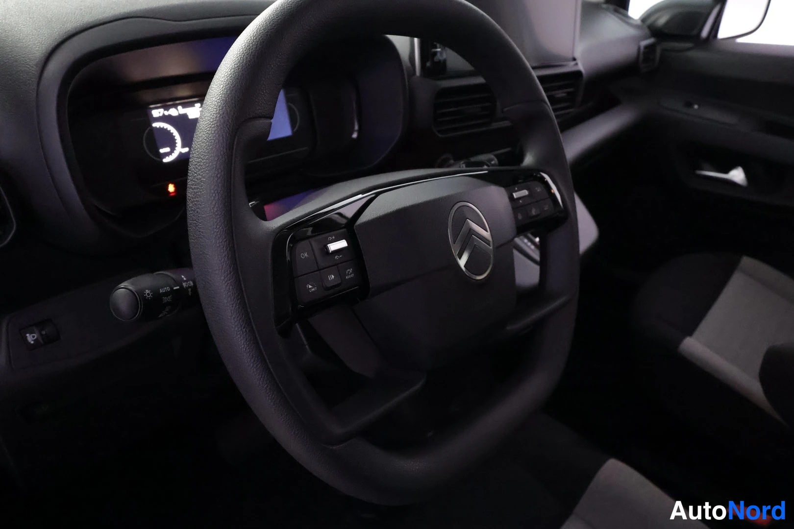 Muu: Ohjauspyörä lähikuvassa Citroën-logolla ja multitoiminnoilla, mittariston taustalla.