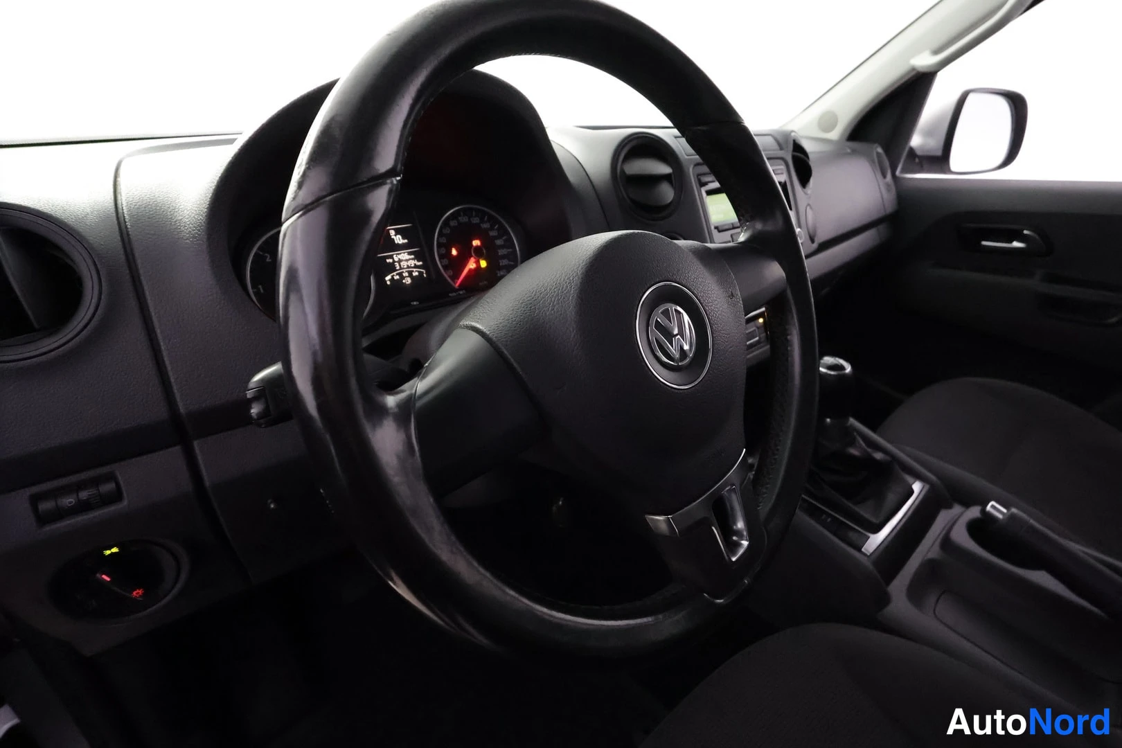 Sivulta: Volkswagen-merkkiohjauspyörä, mittaristo, kojetaulu ja manuaalivaihteen vaihdekeppi keskikonsolissa.