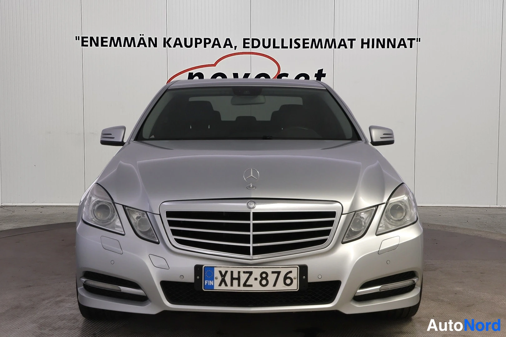 Edestä: Hopeisen Mercedes-Benz-sedan keula suoraan edestä: grilli, ajovalot ja etupuskurin rekisterikilpi.