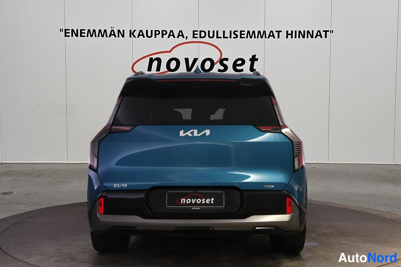 Takaa: Sinivihreä Kia EV9 suoraan takaa kuvattuna valkoisella studiotaussilla; takaluukussa KIA-merkki ja EV9-tunnus, puskurissa punaiset heijastimet.