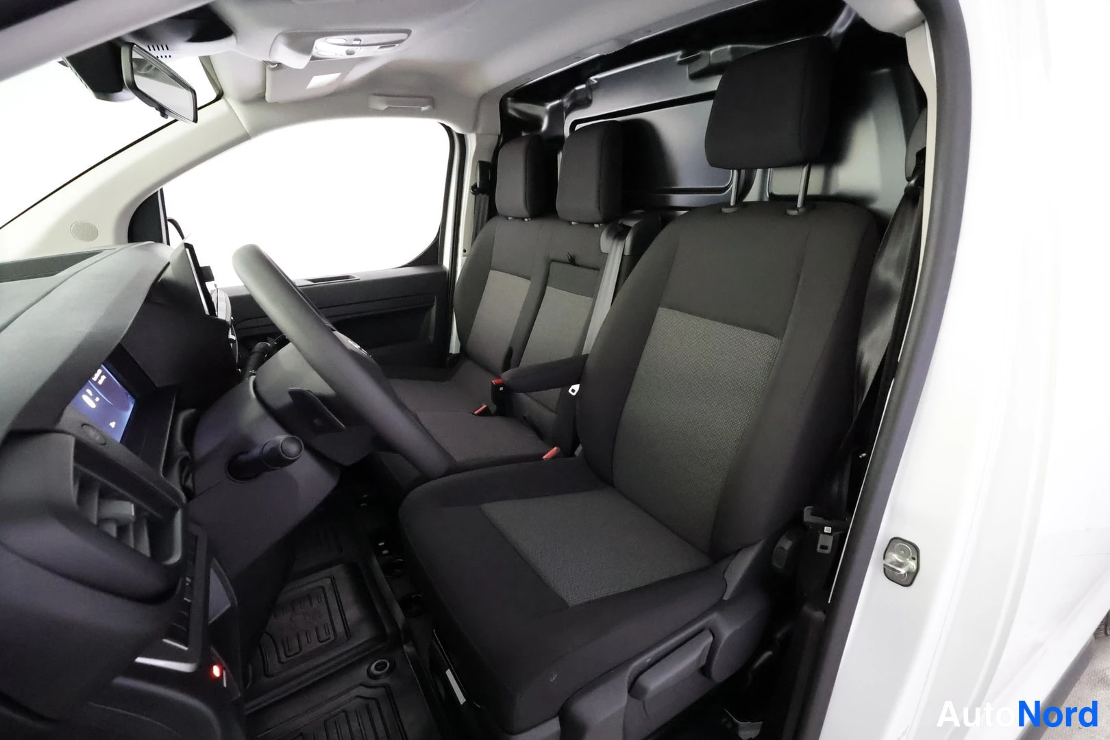 Etuistuimet: Interior shot from open door showing three front seats in dark grey fabric. Driver's seat (left), middle seat and passenger seat (right). Central armrest betwee