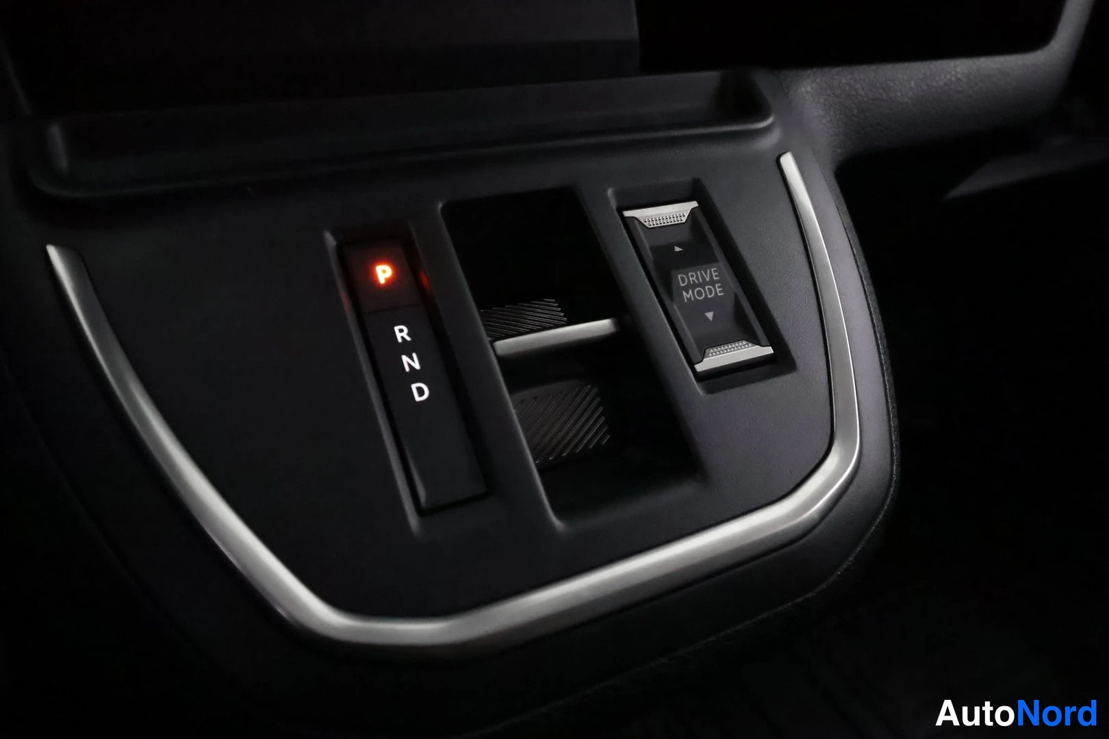 Yksityiskohta: Vaihteenvalitsimen R-N-D kytkin keskikonsolissa, P-valo päällä, DRIVE MODE -painike.