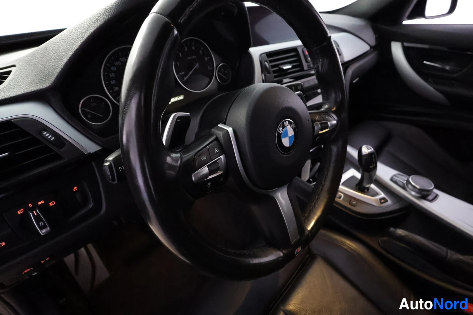 Muu: Ohjauspyörän ja kojelaudan näkymä; BMW-merkki pyörän keskiössä, mittaristo ja vaihtokeila näkyvät taustalla.