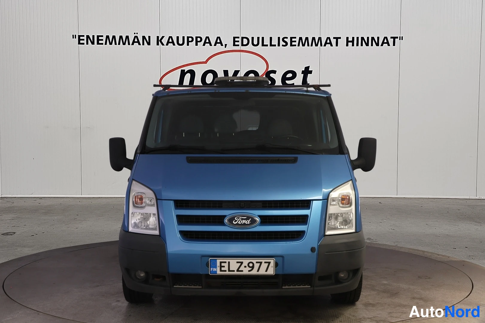 Edestä: Sininen pakettiauto suoraan edestä kuvattuna, Ford-merkki etusäleikössä, rekisteritunnus.