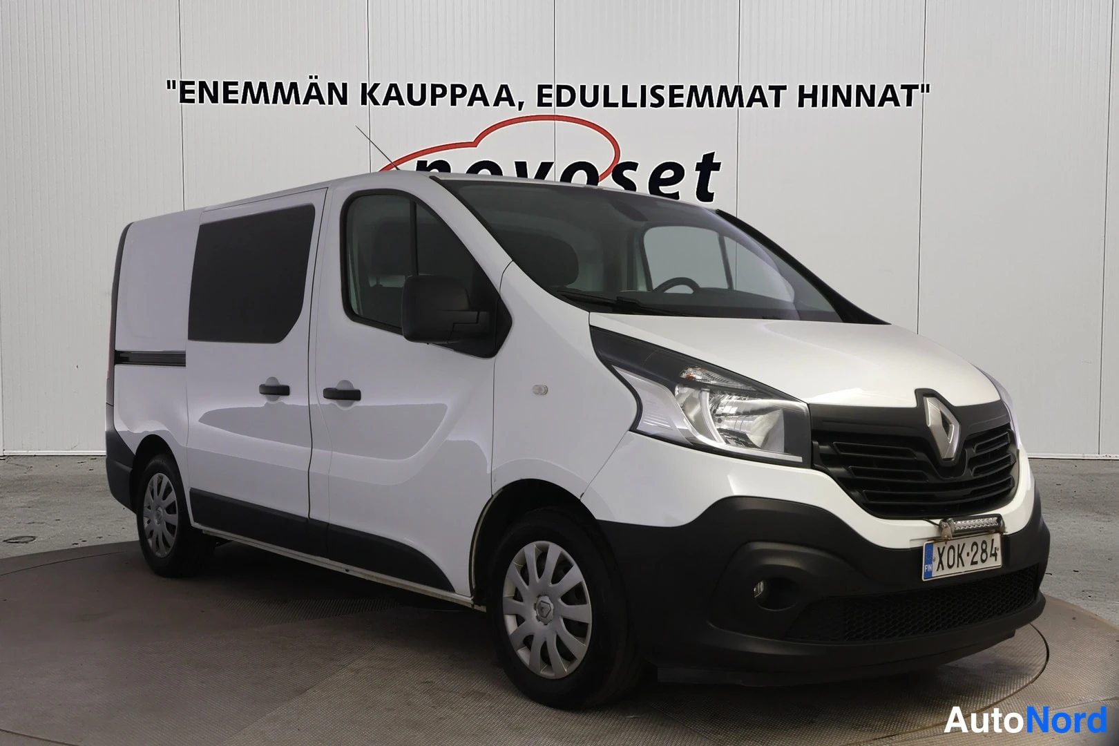 Etuviisto, nokka oikealle: Valkoinen pakettiauto etukulmakuvassa: keula oikealla, kylki ja takapyörä näkyvät vasemmalla, rekisterikilpi.