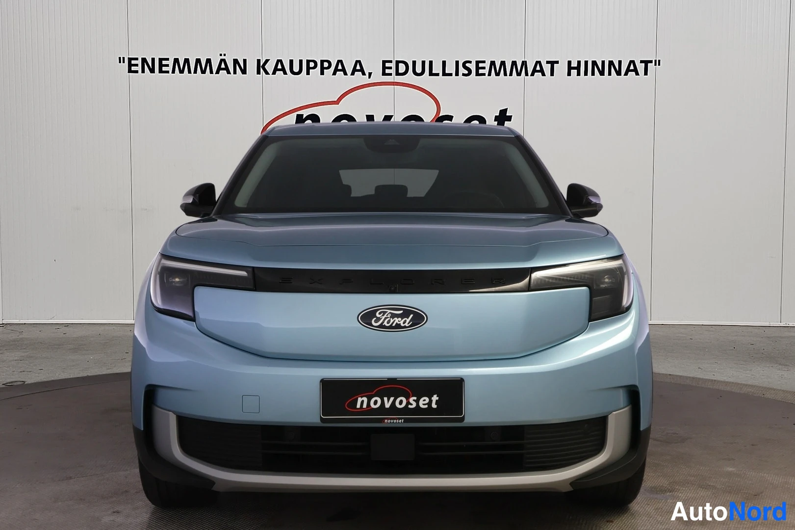 Edestä: Direct front view of a light blue Ford Explorer showing headlights, grille area with Ford badge and lower bumper.