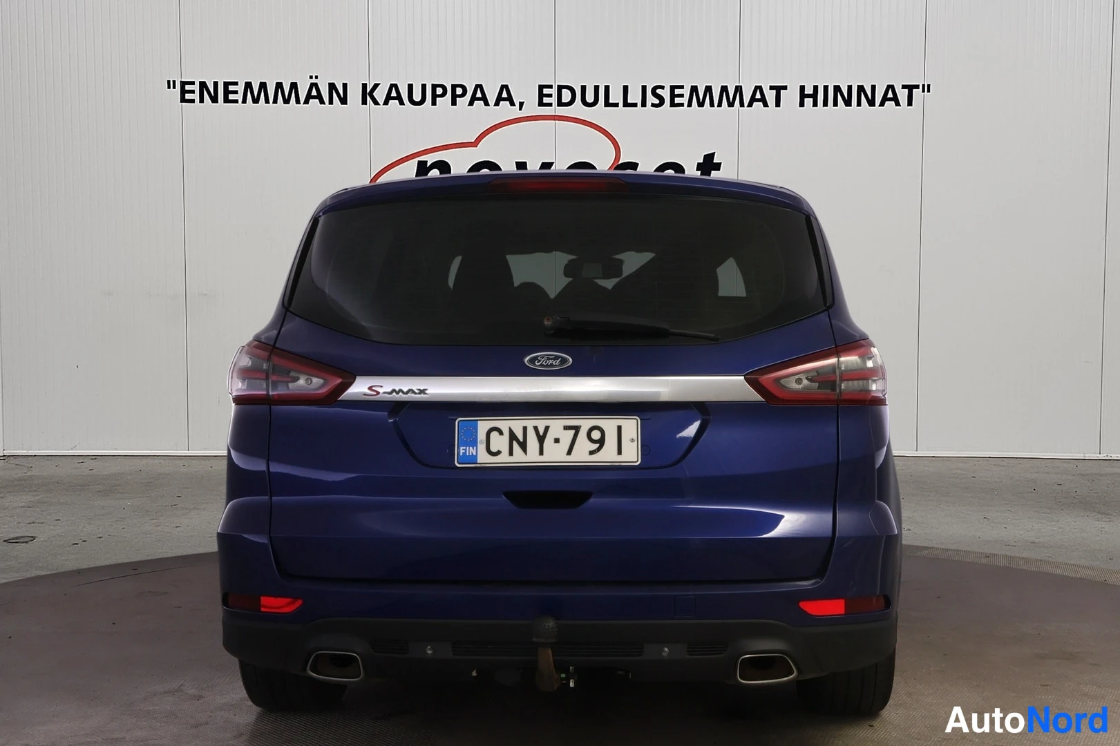 Takaa: Tummansinisen Ford S-Max -auton perä suoraan takaa kuvattuna; takaluukussa Ford- ja S-MAX-merkit, rekisterikilpi, puskurin alla vetokoulu.