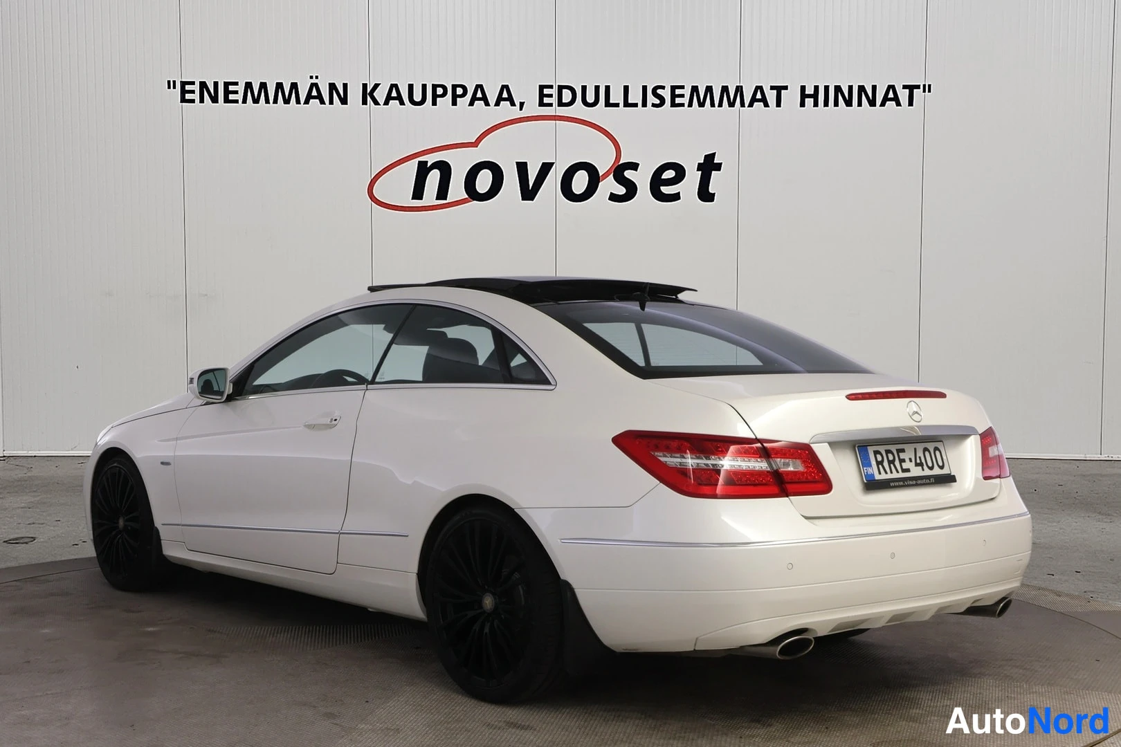 Takaviisto: Valkoinen Mercedes-Benz E-coupé kuvattuna takaa oikealta kolmen neljäsosan kulmasta. Punaiset takavalot, kattoluukku auki-asennossa ja mustat kevytmetallivantee