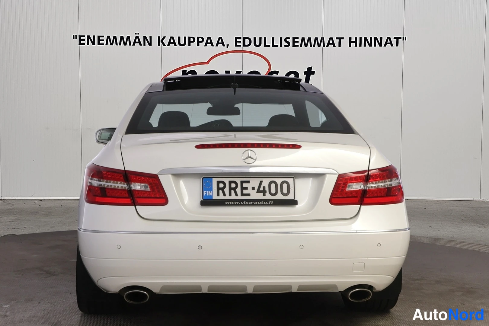 Takaa: Valkoinen Mercedes-Benz E-coupé kuvattuna suoraan takaa. Punaiset takavalot, Mercedes-tähti tavaratilan kannessa, kaksi kromista pakoputkea ja rekisterikilpi.
