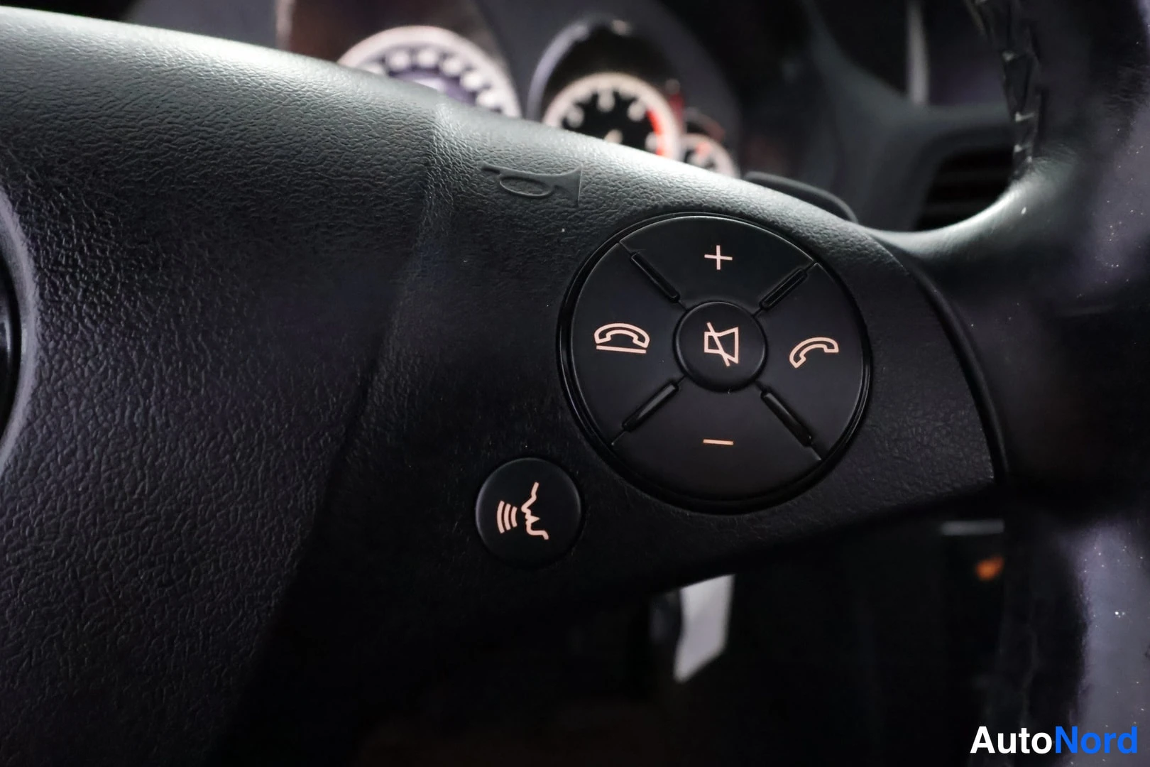 Edestä: Lähikuva Mercedes-Benzin ohjauspyörän oikeasta painikeryhmästä: äänenvoimakkuuden, puhelun ja ääniohjauksen painikkeet mustalla pinnalla.