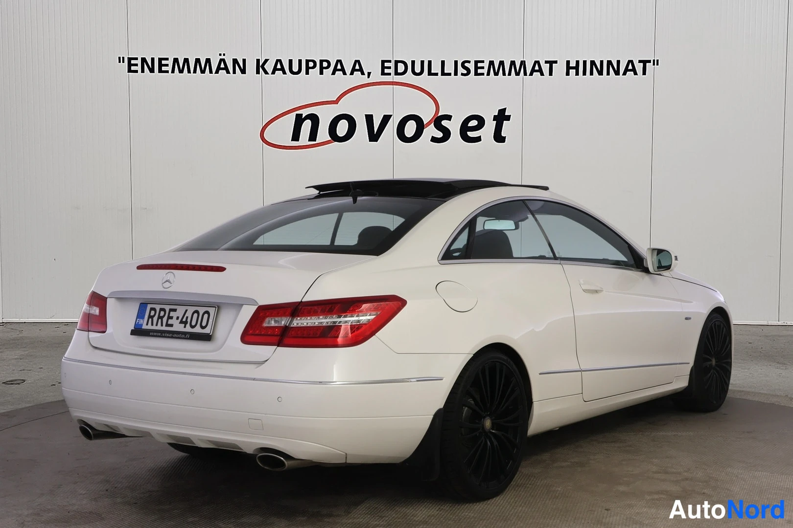 Takaviisto: Valkoinen Mercedes-Benz E-coupé kuvattuna takaa vasemmalta kolmen neljäsosan kulmasta. Punaiset takavalot, mustat kevytmetallivanteet, tumma lasikatto ja korin
