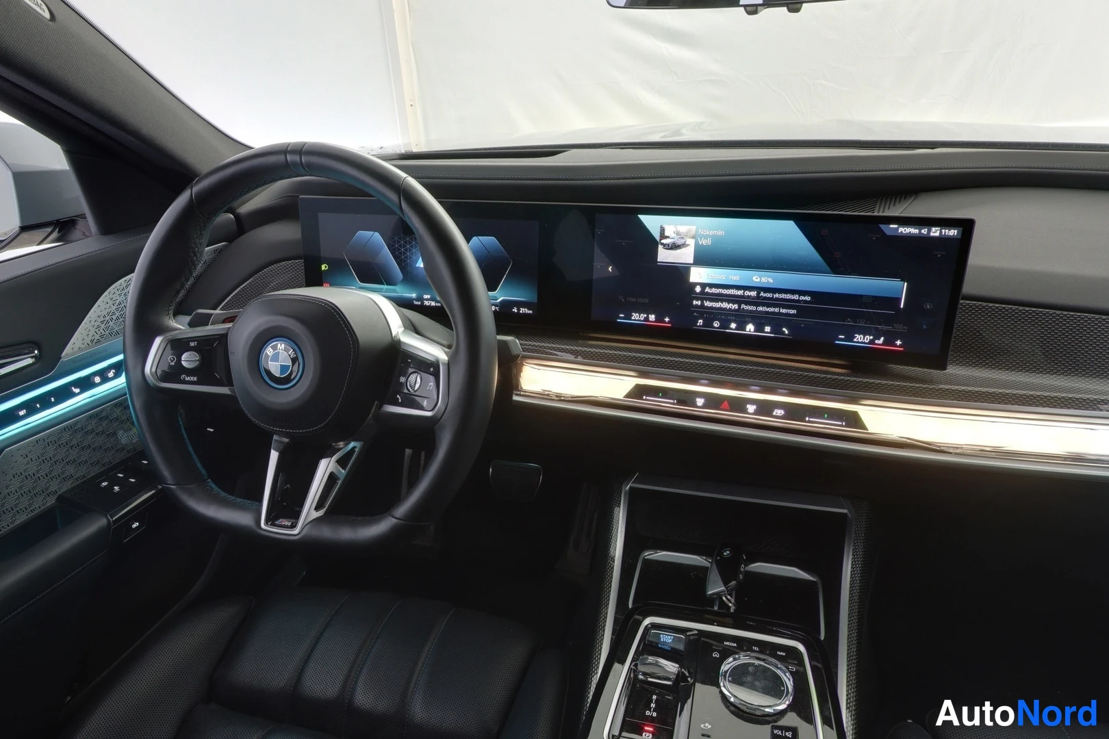 Muu: Ohjaamon lähikuva: BMW-ohjauspyörä, laaja kaarreinostonäyttö radion ja lämpötilojen kanssa, sininen korivalaistus oveen ja metallinen iDrive-ohjain keskikonsoli