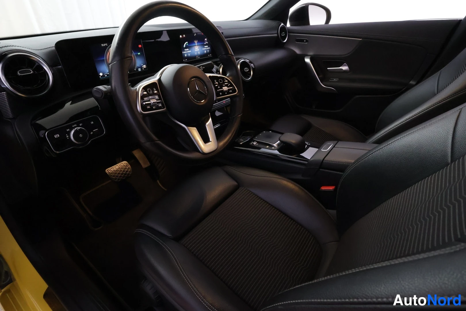 Ohjaamo: Driver's side interior view showing steering wheel with controls, instrument cluster display, dashboard, door panel, and front seat. Part of yellow exterior vis
