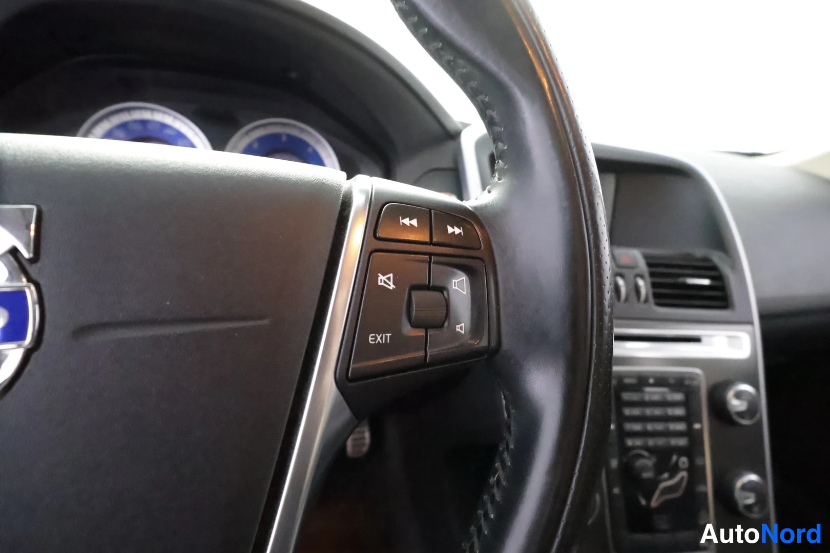 Muu: Volvo-merkitty ratti keskikeskuksella, oikean puolen äänentoisto- ja EXIT-napit sekä kojelauta ja keskikonsoli taustalla.