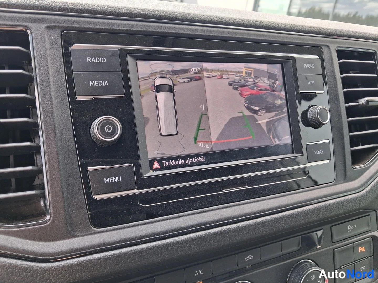 Muu: Ohjaamon infotainment-näyttö, jossa näkyy ympärivaluekamera ja teksti 'Tarkkaile ajotietää'. Napit RADIO, MEDIA, PHONE, APP, VOICE ja MENU sekä A/C-kytkin.