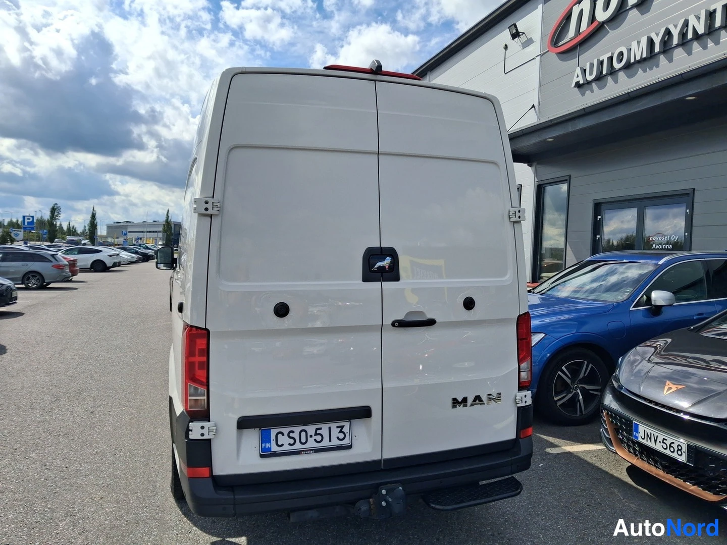 Takaa: Valkoinen pakettiauto suoraan takaa kuvattuna; kaksoisovet, MAN-teksti ja rekisteritunnus CS0-513 näkyvissä. Taustalla parkkialue ja autoliikerakennus.