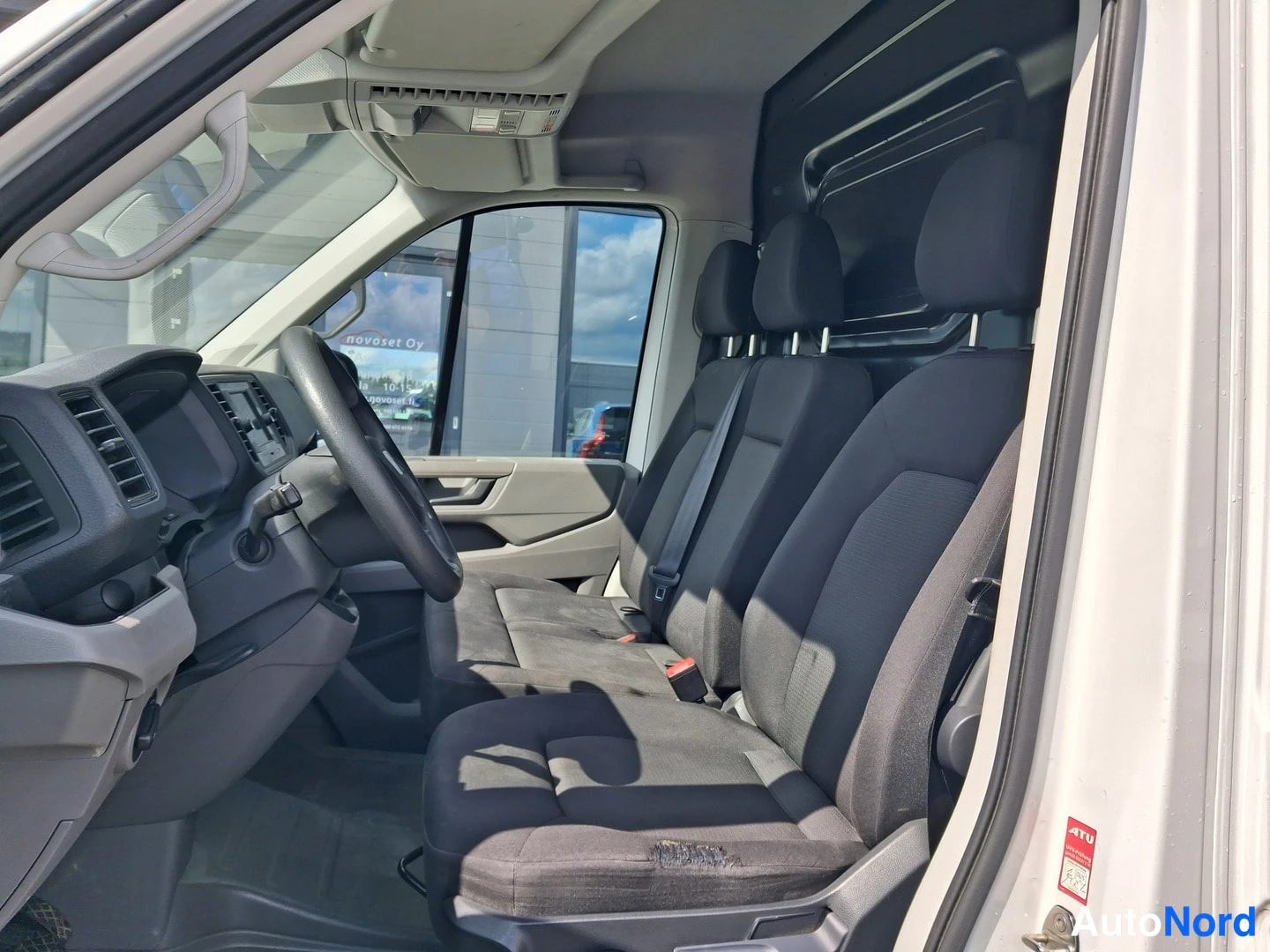 Etuistuimet: Ohjaamon sisäkuva oikean oven kautta. Näkyvissä ohjaamo-ohjainpaneeli ja kolme etuistuinta.