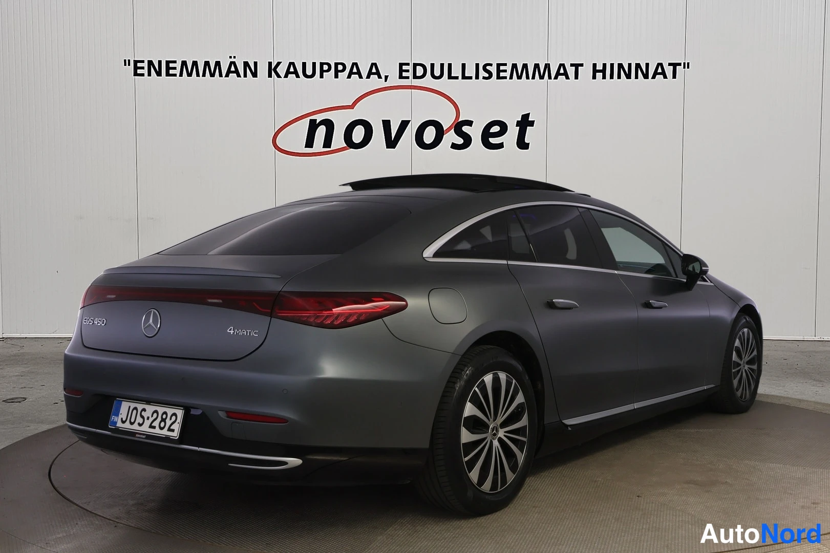 Takaviisto: Harmaan sedanin takakulma kuvattuna oikealta takaa; takaluukussa merkinnät EQS 450 ja 4MATIC, rekisterikilpi, tumma lasikattopaneeli näkyy katolla.