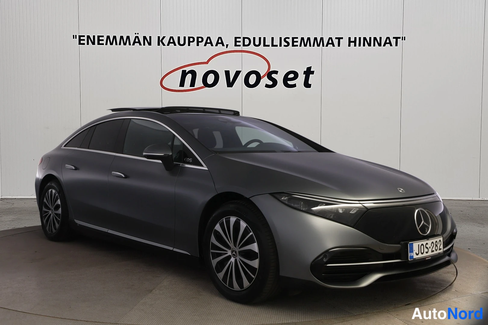 Etuviisto, nokka oikealle: Harmaa Mercedes-Benz -sedan etu-kulmakuvassa sisätiloissa, kylki ja keulä näkyvät, rekisterikilpi.