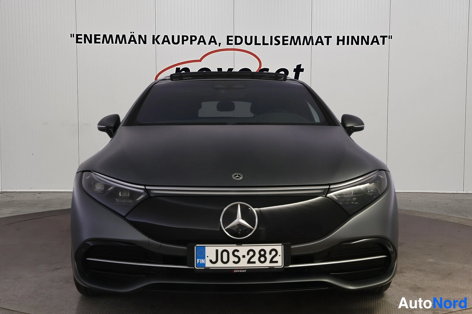 Edestä: Suora etukuvä harmaasta Mercedes-Benz -sedanista, kilpi, valkoinen studio-tausta.