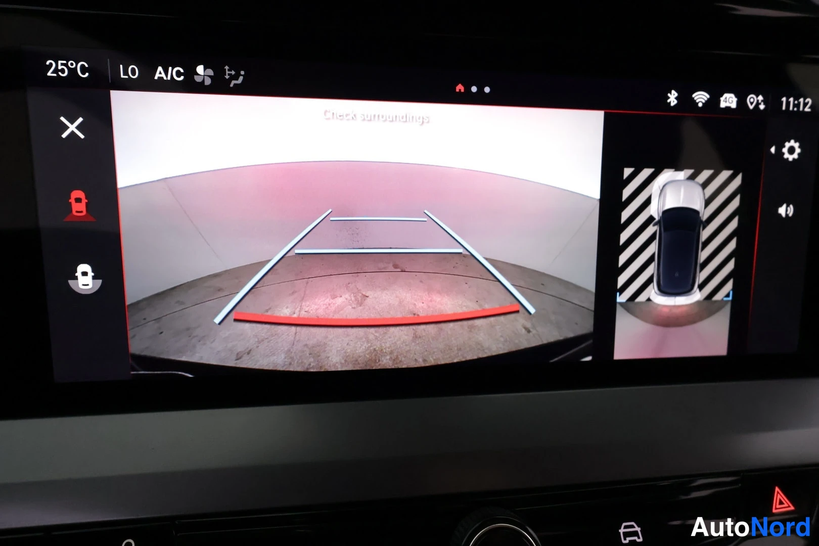 Ohjaamo: Infotainment display showing a split-screen view with a reverse camera feed on the left (showing parking guidelines and a wall) and a top-down surround-view gra