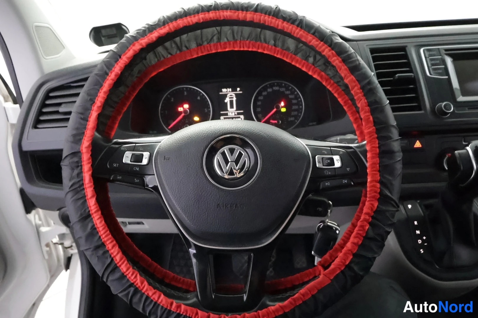 Muu: Ohjauspyörä punaisella ja mustalla tukepeittimellä Volkswagen-merkillä keskellä; taustalla kojelaudan mittaristo, infonäyttö (10:21, P) ja radiopaneeli.