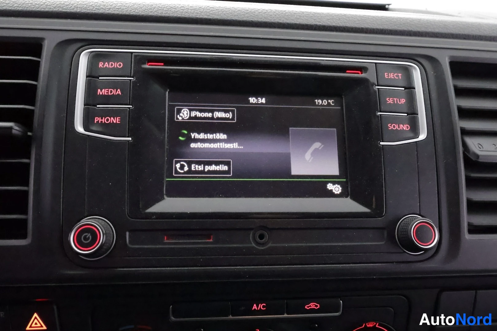 Muu: Kojelaudan radionäyttö, jossa näkyy iPhone (Niko) -yhdistämisruutu ja A/C-painike.