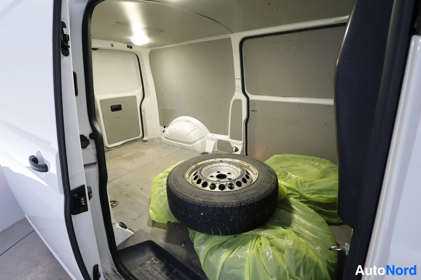 Muu: Pakettiauton kuormatila liukuväyläovelta katsottuna: paneeliseinät, vararengas ja vihreitä muovipusseja lattialla.