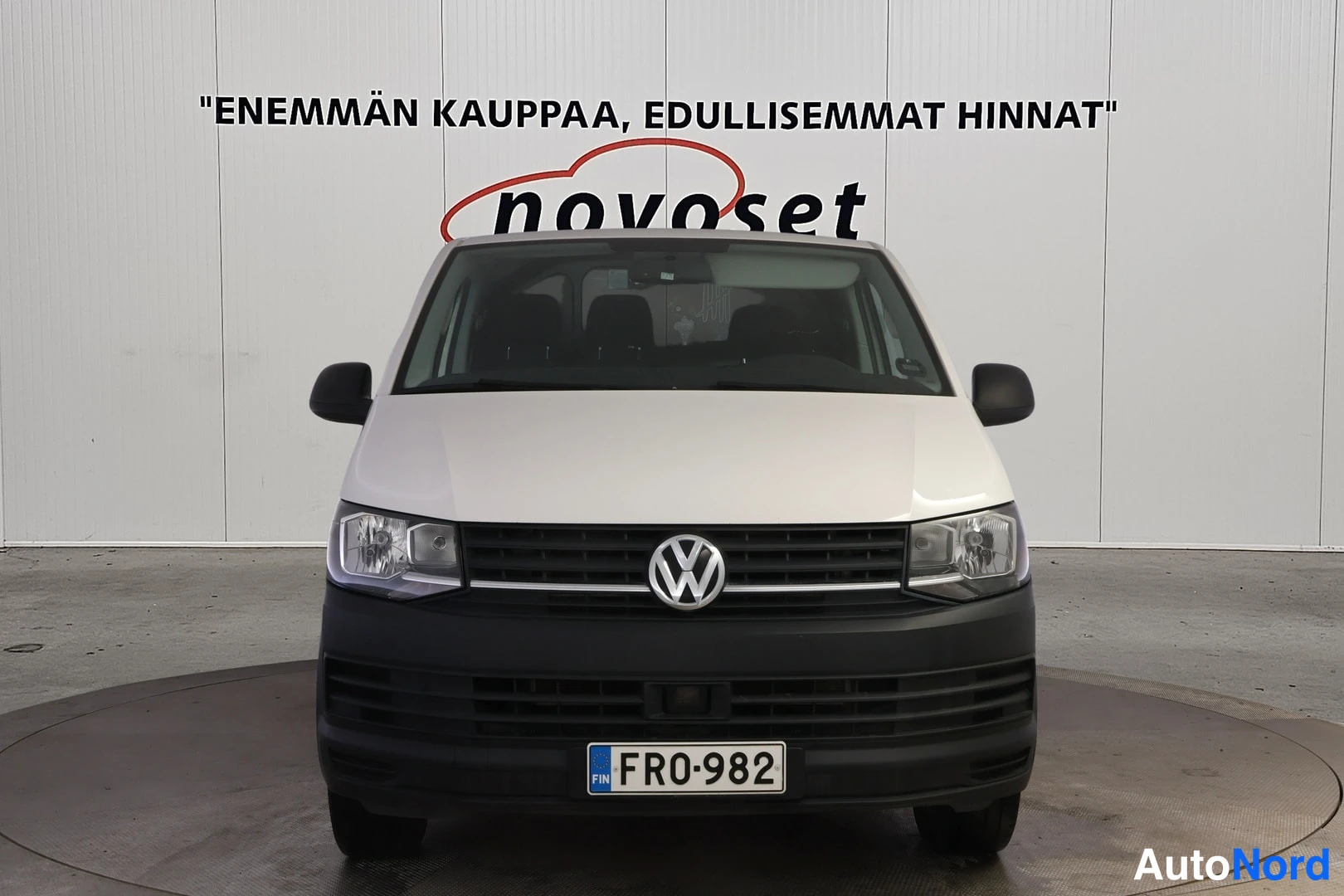Edestä: VW Transporter -pakettiauto suoraan edestä valokuvattuna, valkoinen kori ja musta etupuskuri, rekisterikilpi.