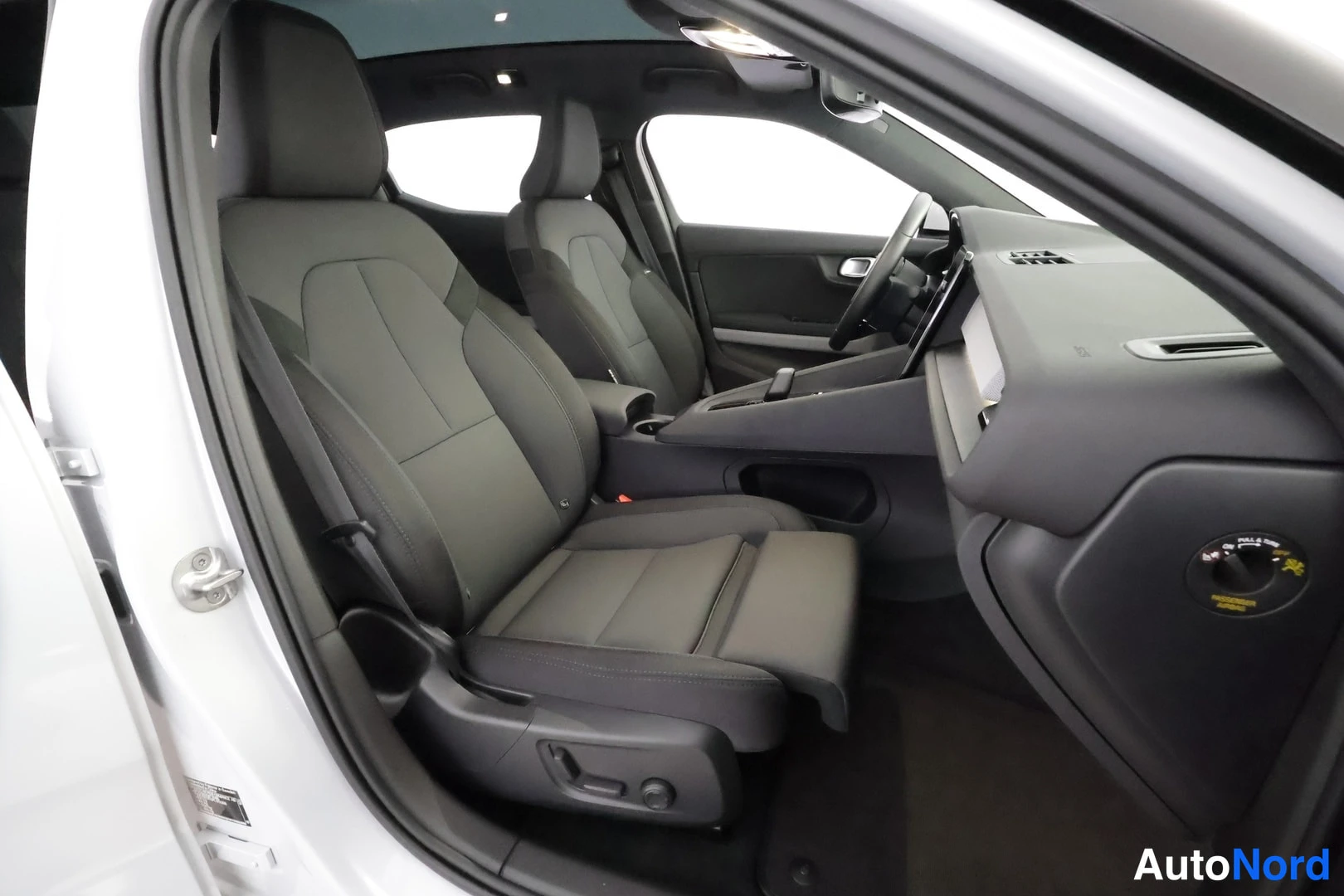 Etuistuimet: Cabin interior view from the open driver's door. The image shows two front seats in black material, a large central touchscreen infotainment screen, the steerin