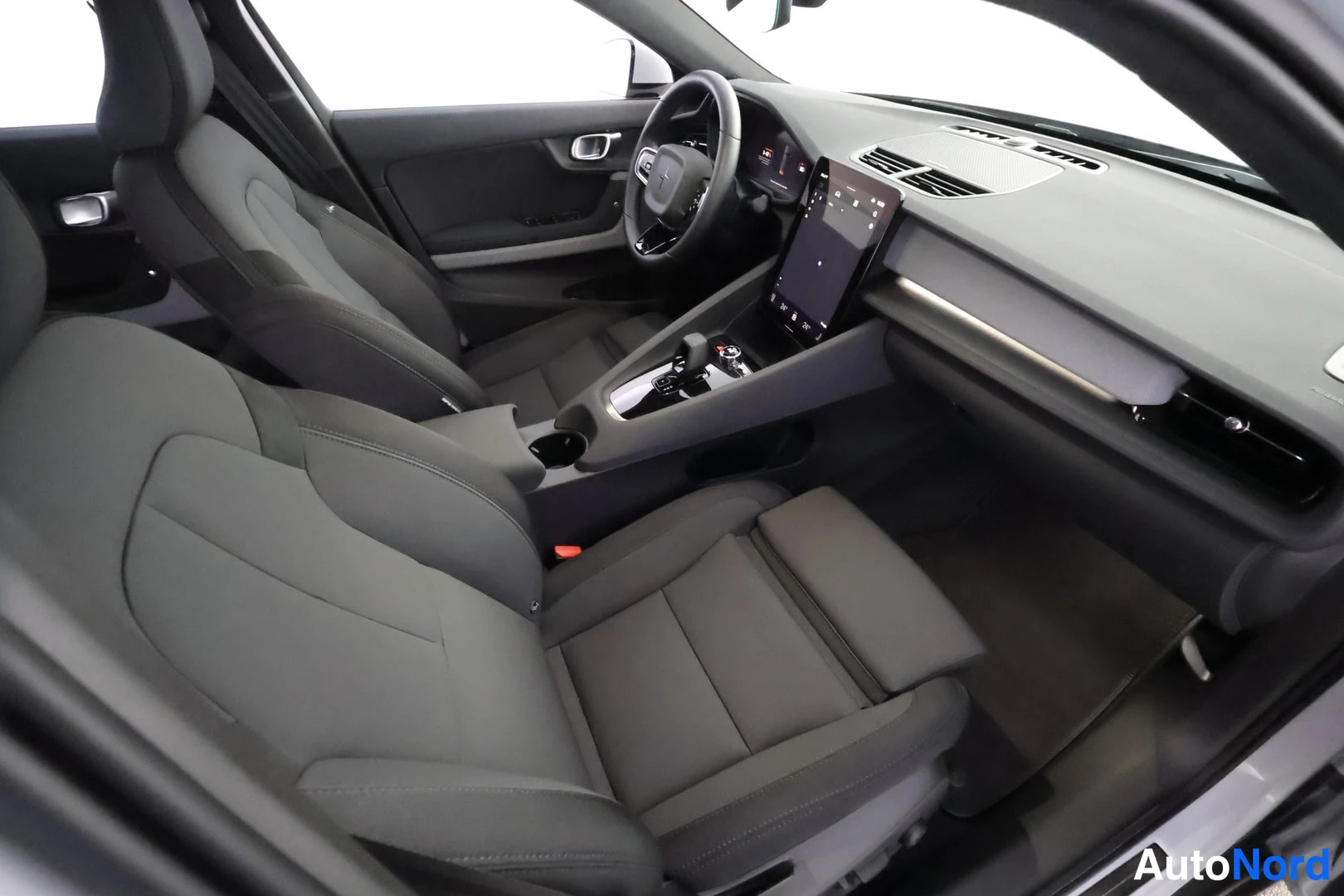 Etuistuimet: High angle interior view of the front cabin showing the dashboard, steering wheel with central logo, vertical infotainment screen, and front seats.