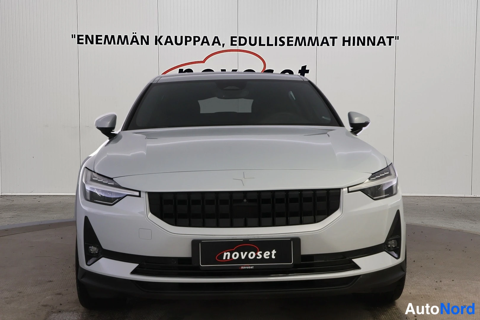 Edestä: Valkoisen Polestar 2 -sähköauto etunäkymä, kuvattu etuosasta suoraan edessä.